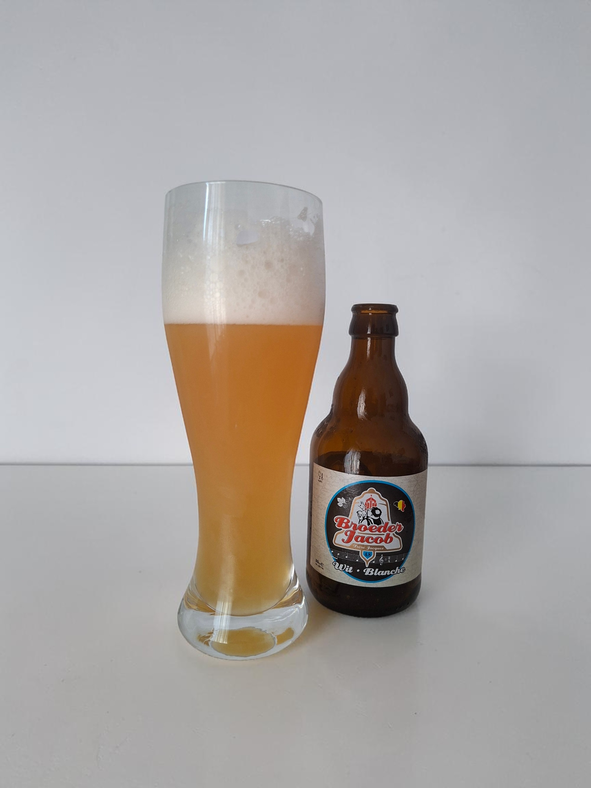 Witbier poured into a tall glass beside its bottle, showing its cloudy golden color and white foam head, on a clean white background